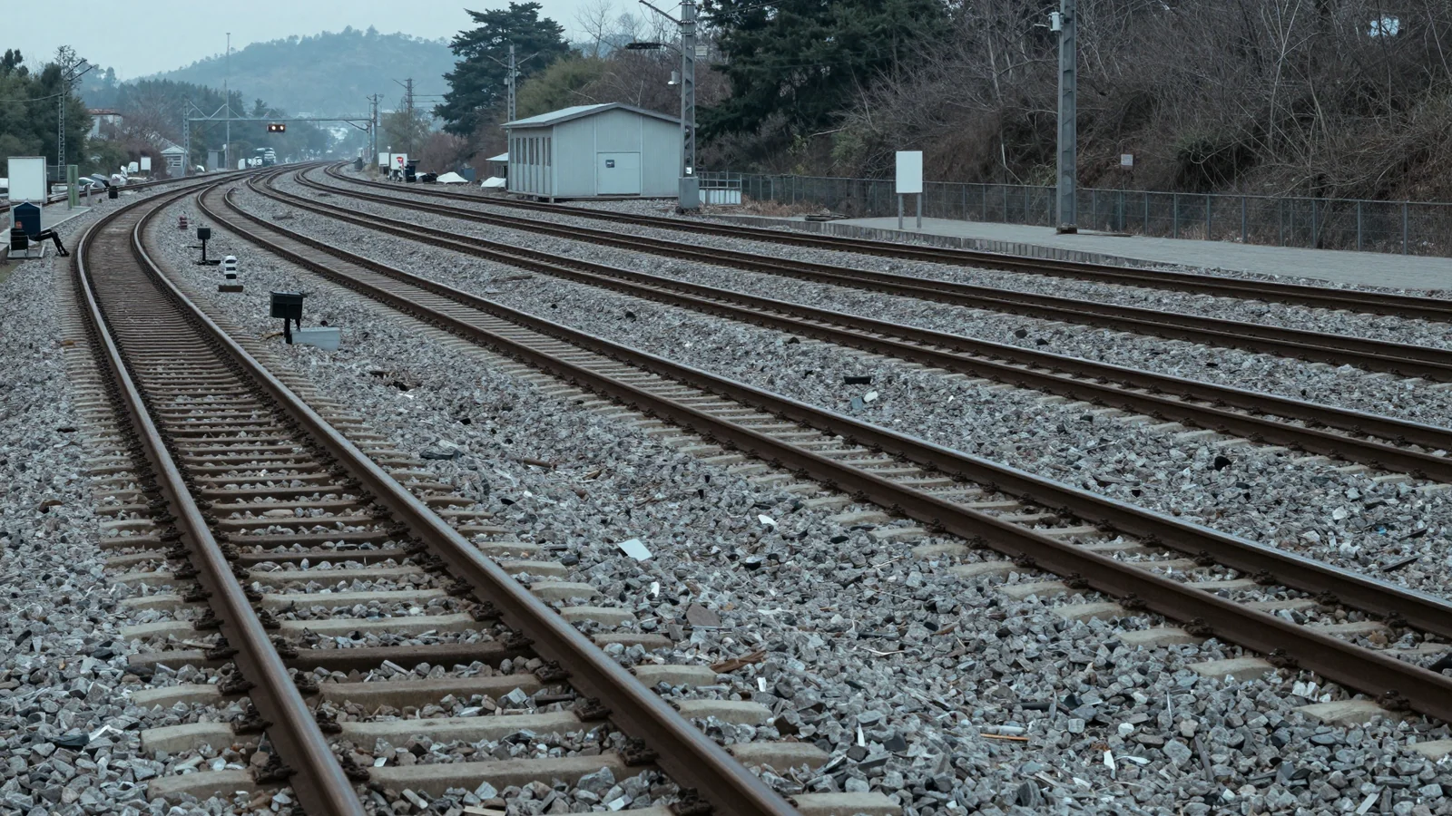 Empty railway tracks and switches curving past a small grey maintenance building toward wooded hills.
