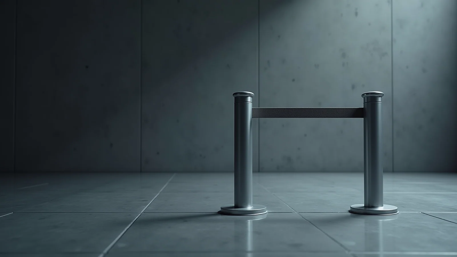 Two steel stanchion posts standing on a polished concrete floor with a dark belt drawn taut between them, in a dim room lit cold from above.