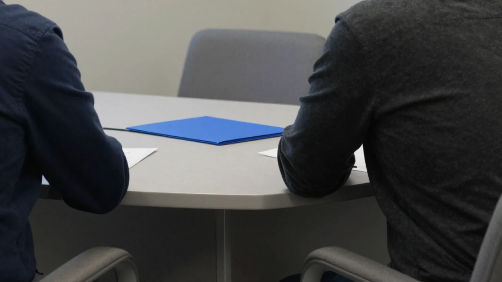 Navy and charcoal sleeves surround a pale consultation table with a closed blue folder; both heads are outside the frame.