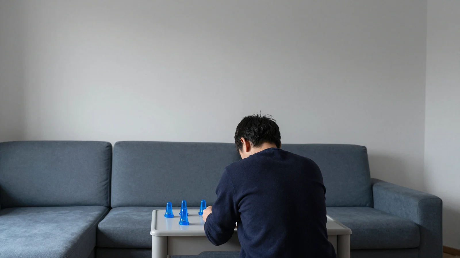 An adult seen from behind leans over small blue light toys on a low grey table beside a blue-grey sofa.